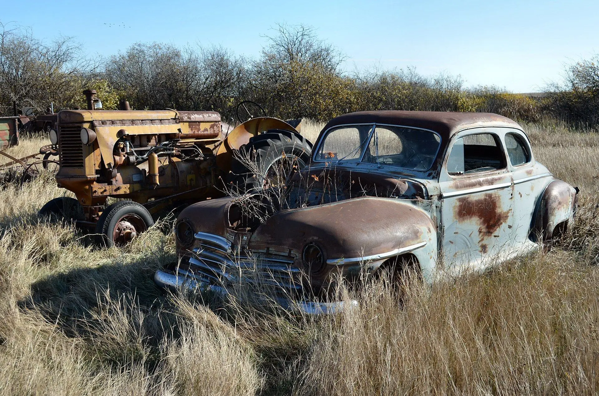 Abandoned Plymouth coupe and tractor in grass