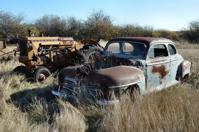 Abandoned Plymouth coupe and tractor in grass
